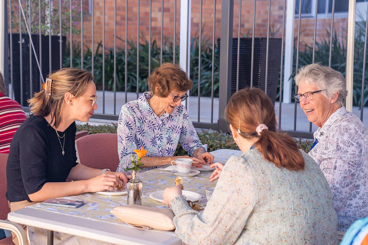 Attendees sit at a table talking and laughing with each other while enjoying tea and food.