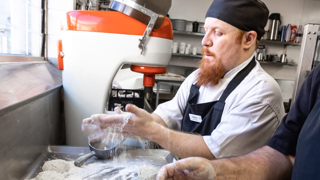 Nathan, a Cookery Nook team member, is shown busily rolling dough with flour.