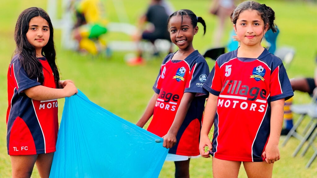 Three young girls in soccer gear help clean up.
