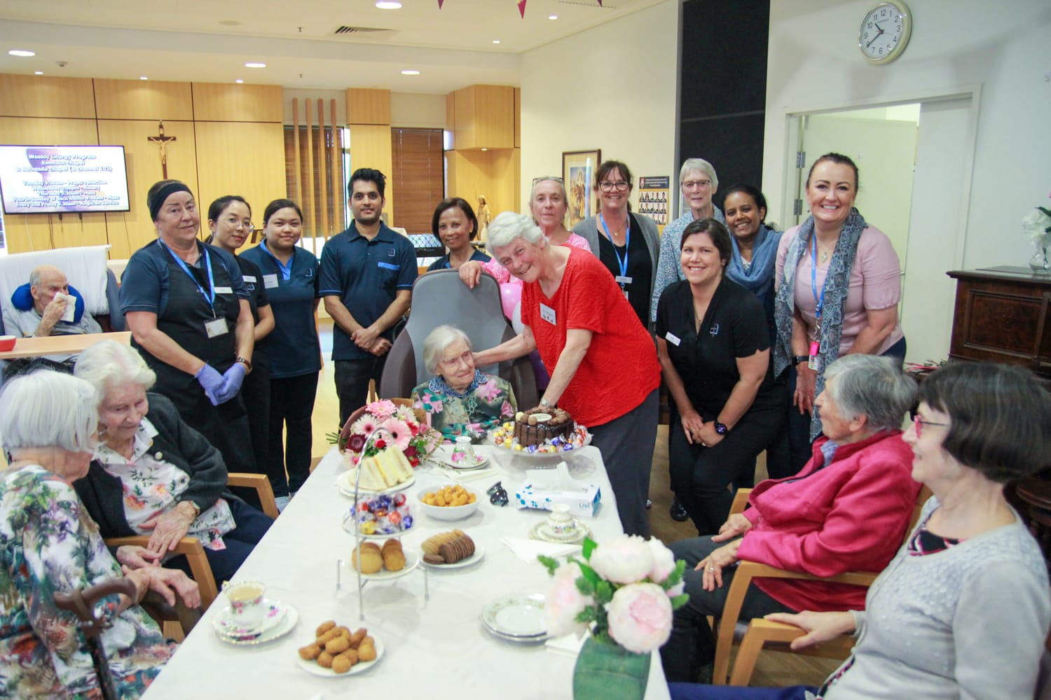 Aged care team members and residents crowd Sister Jeanne to sing Happy Birthday.