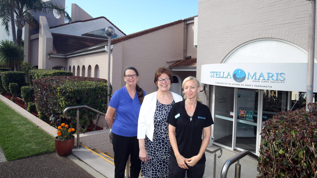 Three Stella Maris team members stand outside the facility smiling at the camera.