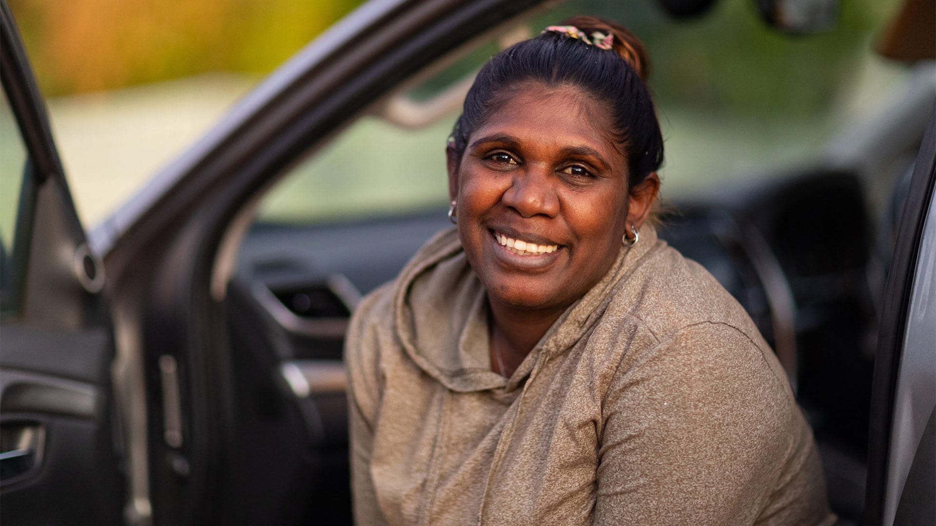 A woman sits in the front seat of a car smiling at the camera.