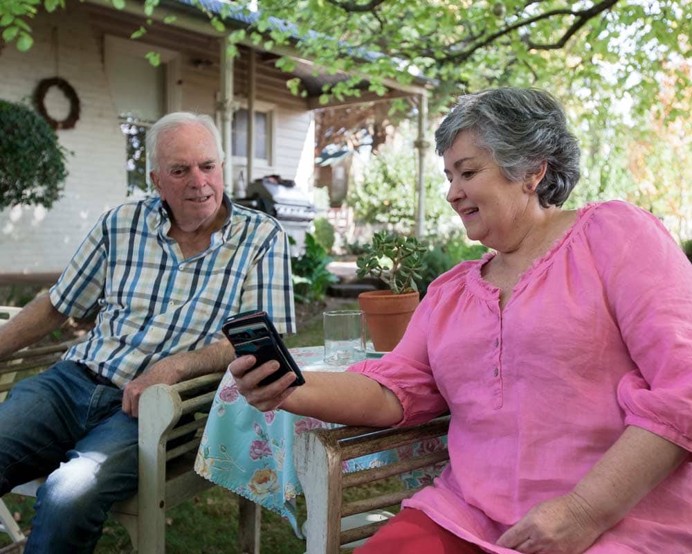 An older couple relaxing in the garden with a demonstration of social media on a mobile device
