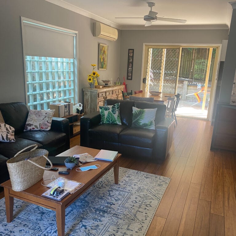 This image shows the living area's large window, aircon and wooden flooring. You can see a large glass sliding door leading to the back yard.