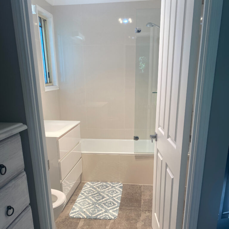 The ensuite is shown with its stone tile flooring and white tiled walls. It's modern with a large bathtub and shower and white vanity.