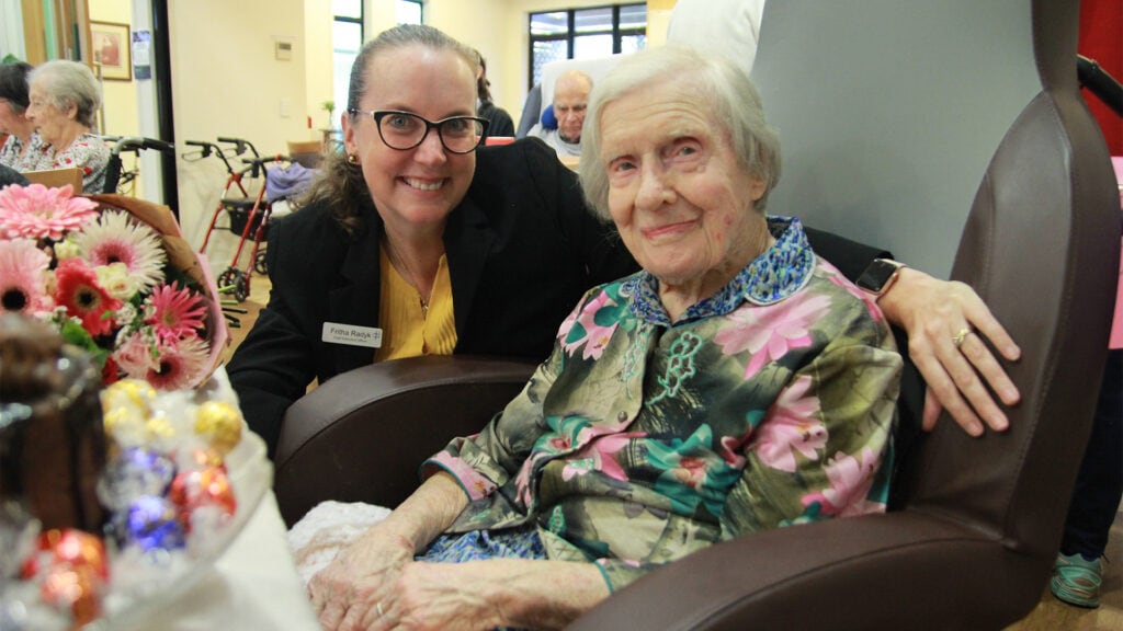 CEO Fritha Radyk and Sister Jeanne smile at the camera infront of Sister Jeanne's birthday cake. Fritha has her arm around Sister Jeanne.