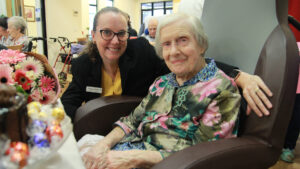 CEO Fritha Radyk and Sister Jeanne smile at the camera infront of Sister Jeanne's birthday cake. Fritha has her arm around Sister Jeanne.