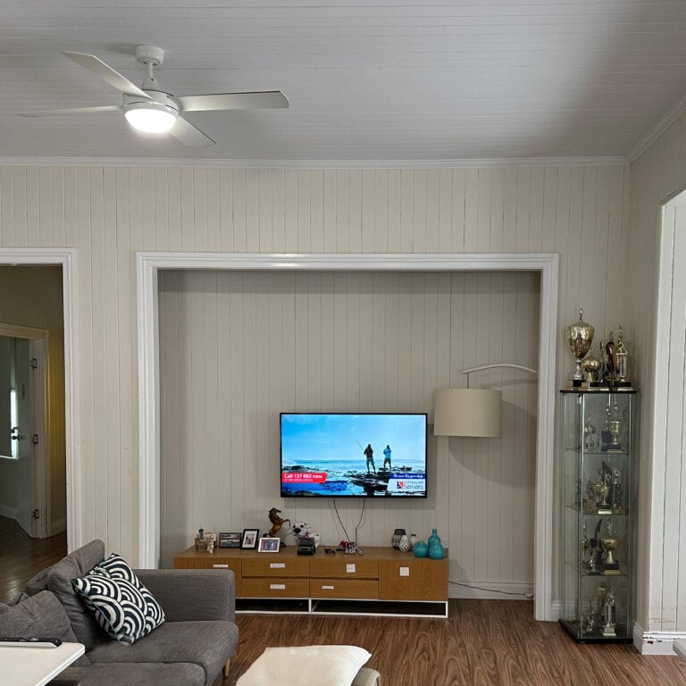 This image shows the large living area of the house. The walls are wooden slats painted cream with white trimmings. The entertainment system is in a shallow but tall alcove in the wall.