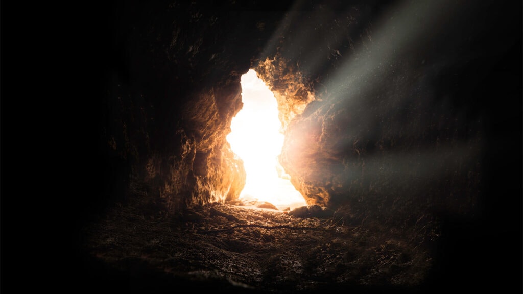 An image of light dramatically piercing through the opening of a dark tomb/cave.