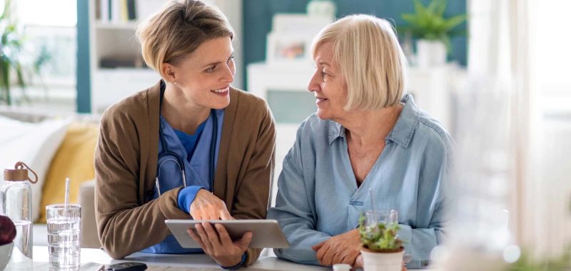 Caregiver or healthcare worker with senior woman patient, using a tablet and explaining.